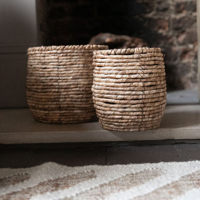 Two brown woven baskets placed in front of a fireplace
