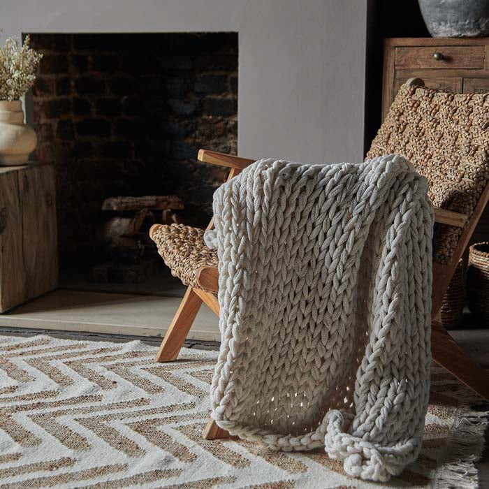 A cream coloured chunky knit throw draped over an armchair.