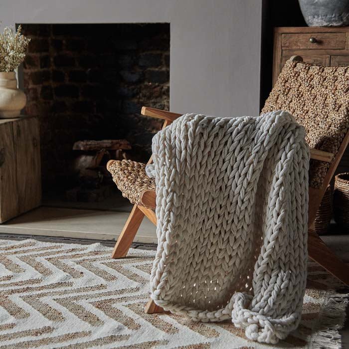 The Baxley Chunky Knit Throw, a cream coloured chunky knit throw draped over an armchair.