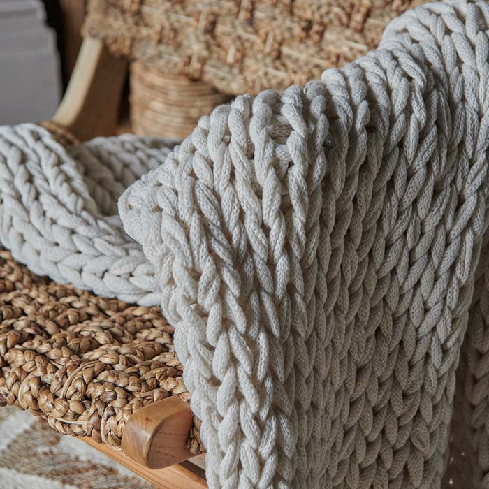 Chunky knit cream throw draped over arm of chair.