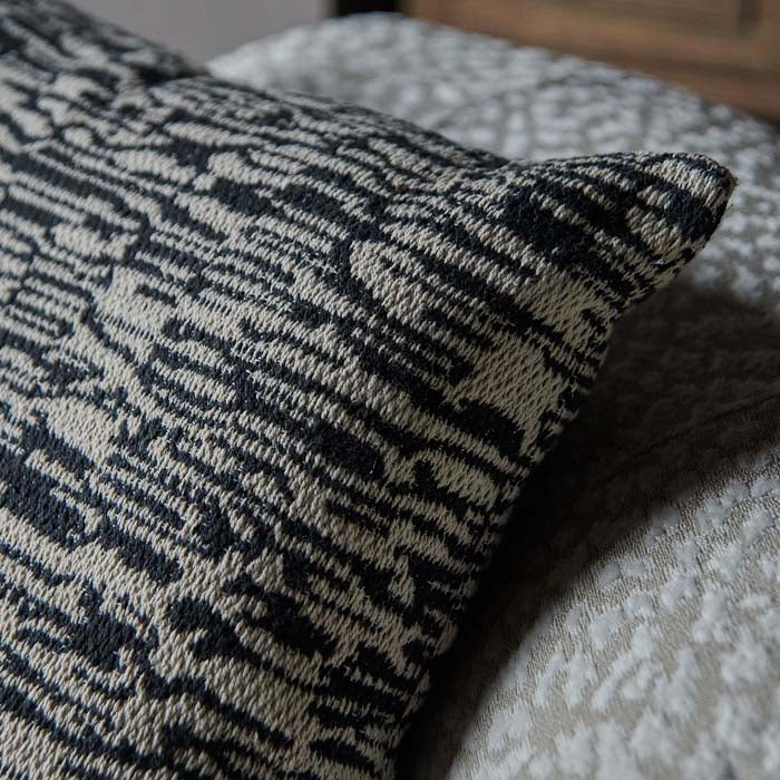 Woven fabric cushion cover in natural and black tones.