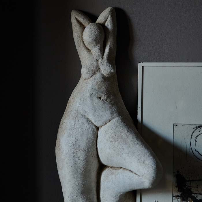 A cement sculpture of a reclining figure, leaning against a wall.