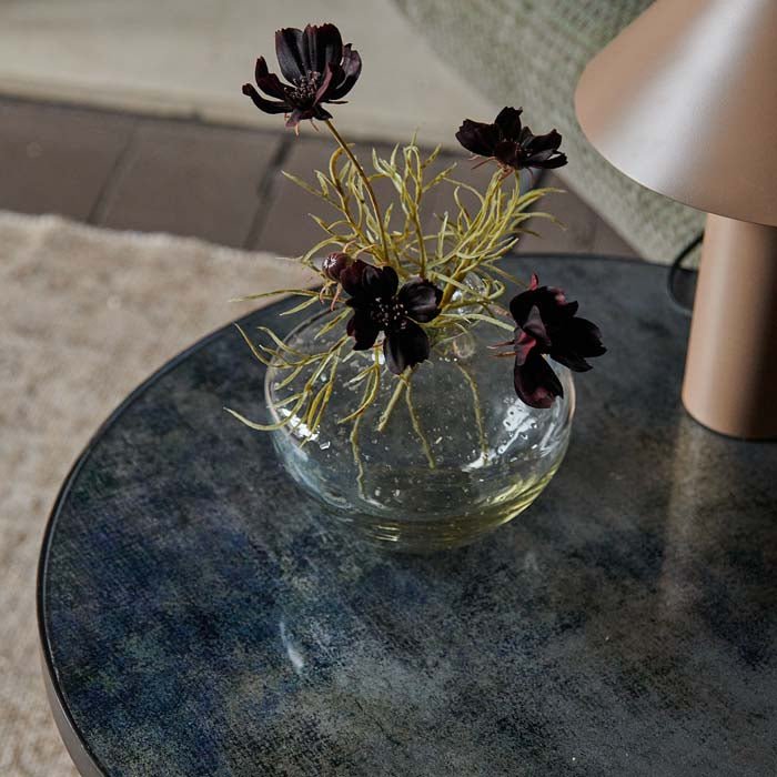 Clear glass vase with dark red flowers sat on a blue glass table