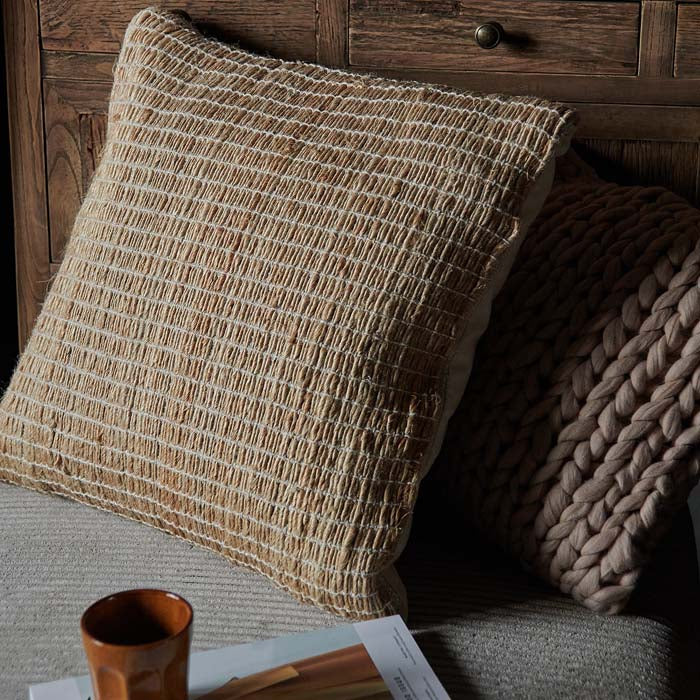 Square woven jute cushion next to pink knitted cushion.