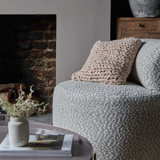 Pale pink square knitted cushion on grey occasional chair.