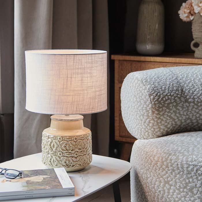 Warm light emitting from a white drum shade on ceramic table lamp.
