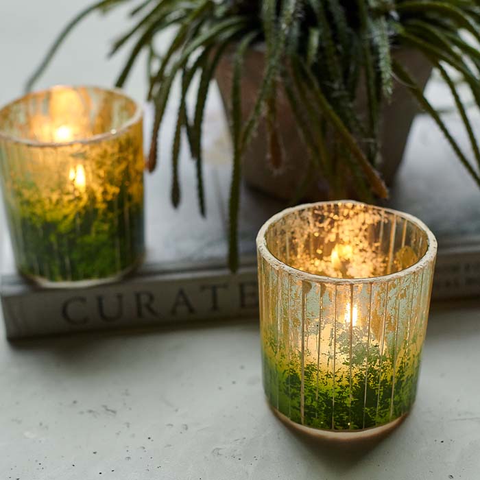 Tow glass votives in a gradient of green with lit tea lights inside