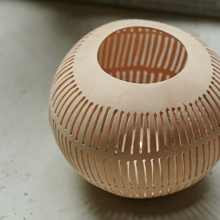 Tealight candle glowing through stripe cut-out design on coconut candle holder.