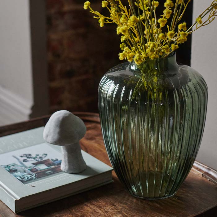 Textured green glass vase sat on a wooden side table