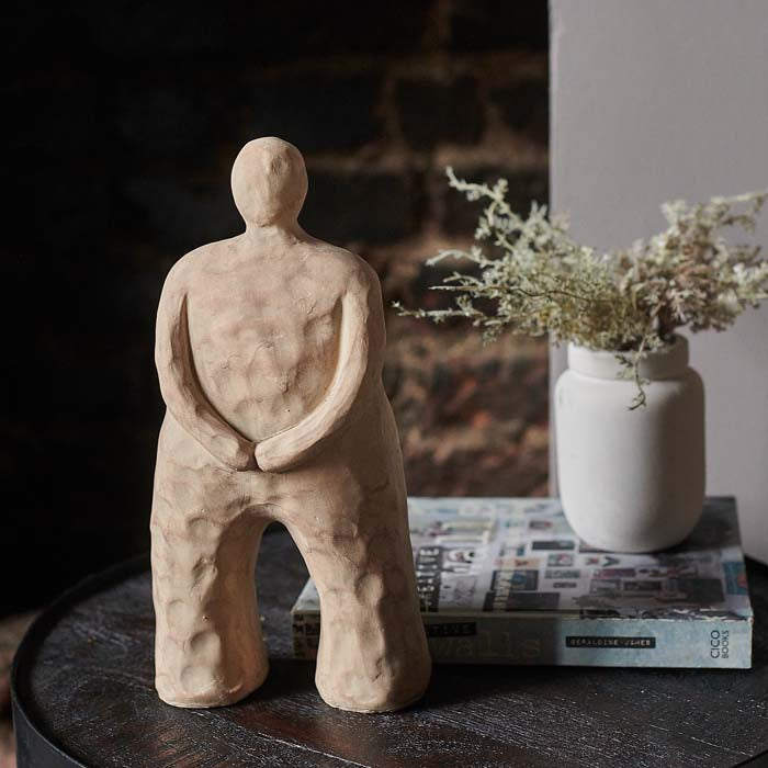 Rustic sandy brown abstract figurative sculpture, with arms curved across body.
