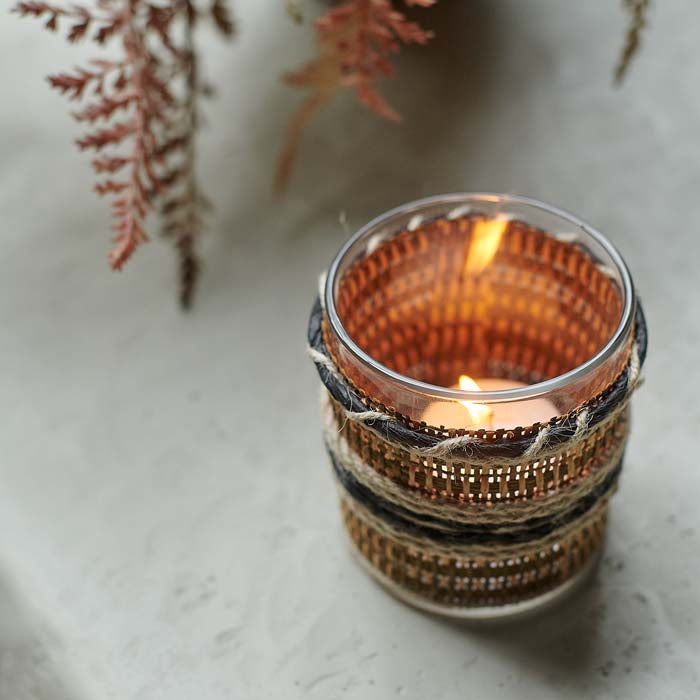 Tealight candle glowing through woven fabric covered glass candleholder.