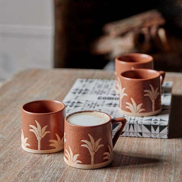 Set of four terracotta-glazed stoneware mugs decorated in palm tree motif.