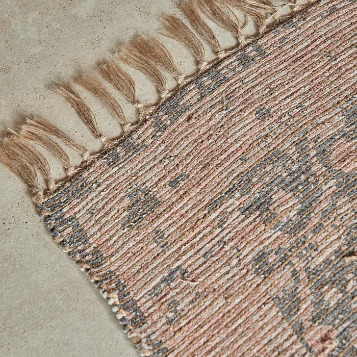 Tasseled edges on a pink and brown woven jute rug.
