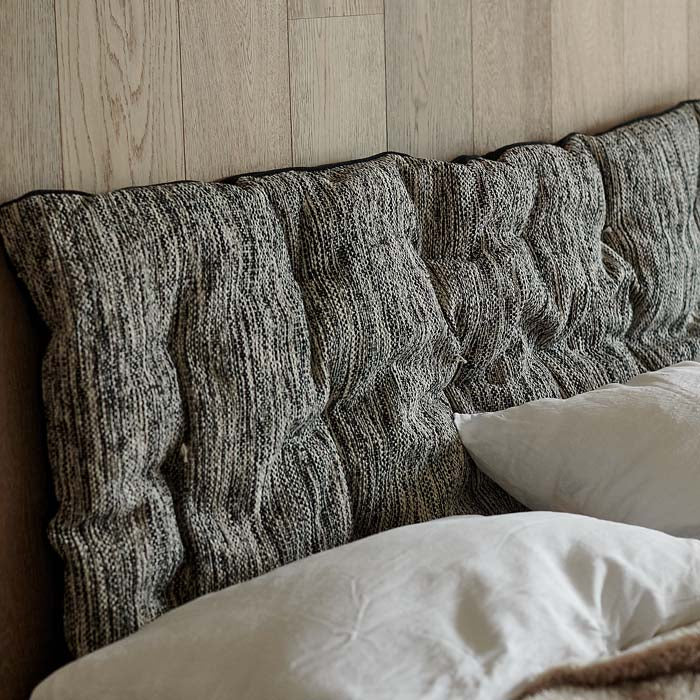 Woven grey cotton headboard cushion leaning against a wall.