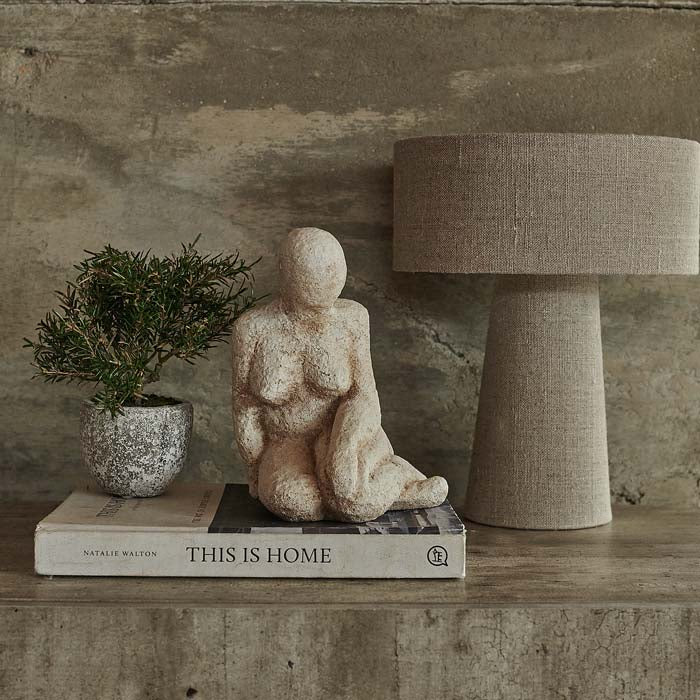 A cement sculpture of a sitting figure looking downwards, displayed on a coffee table book.