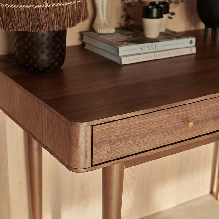 Rounded corners on warm brown wooden desk, and small gold handle on drawer.