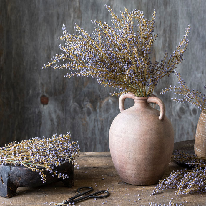 A large bunch of textural purple heather stems in an urn style terracotta vase