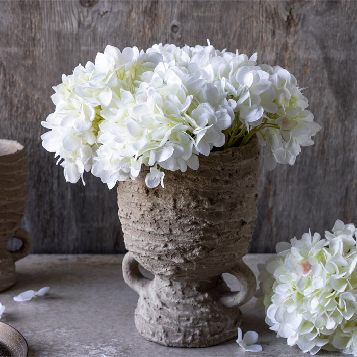 Hourglass shaped vase with five white hydrangea stems inside