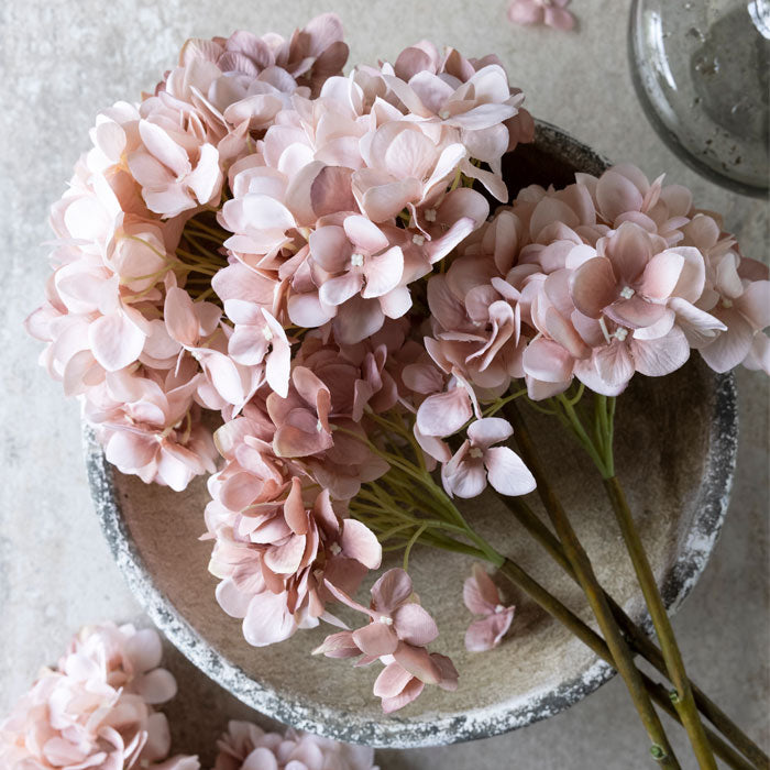 4 artificial hydrangea stems in blush piled up on a large grey bowl