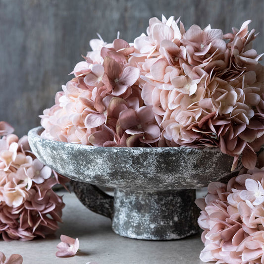 Blush coloured faux hydrangea stems piled up on a wide grey decorative bowl