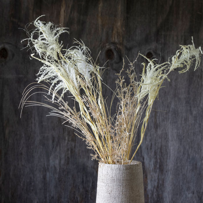 Three feathery cream artificial grass stems in a grey vase