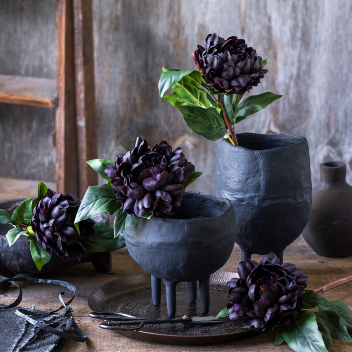 Two black metal vases of different heights filled with purple flowers