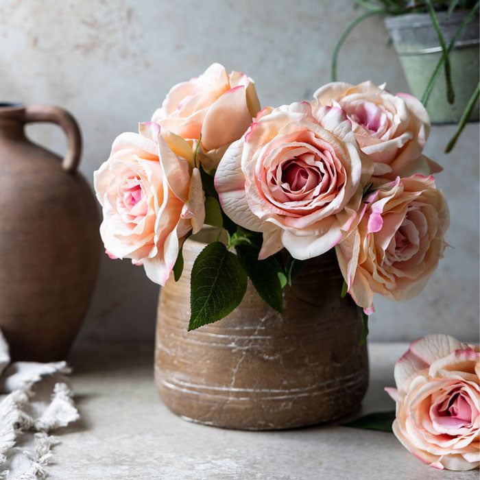 Five coral-blush hued artificial roses placed in a short round vase