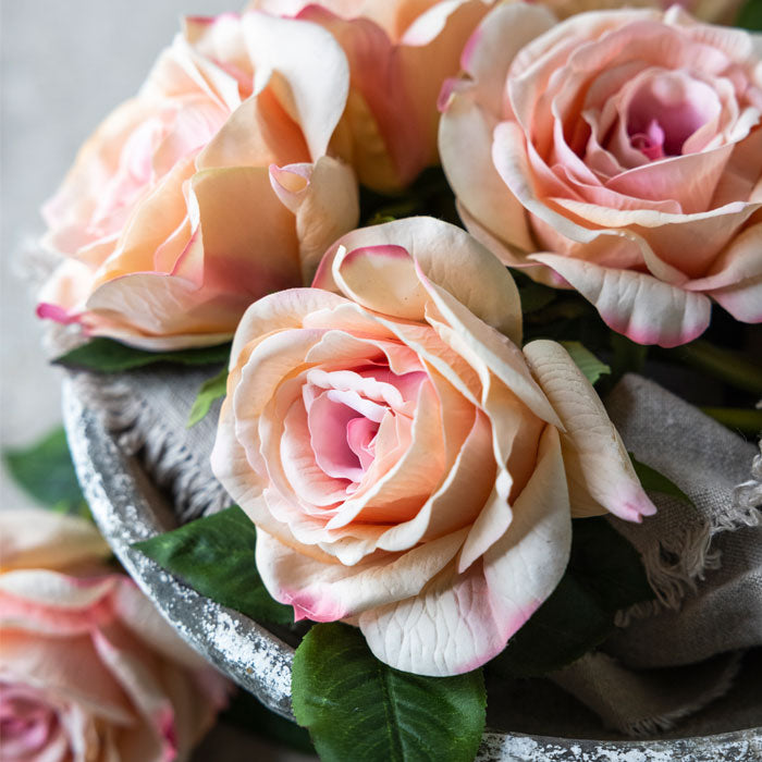 Three artificial blush-coral hued roses resting on a large round tray