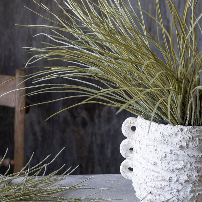 Artificial green spiky grass placed in a textured white vase