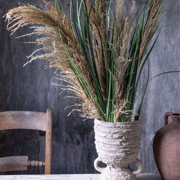Large bunch of dried pampas grass stems with artificial green leaves placed in a grey vase