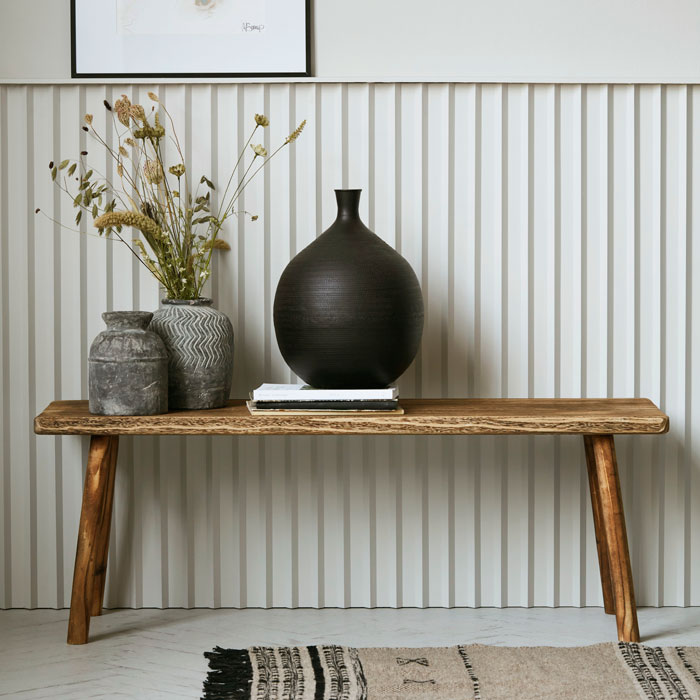 Long wooden bench, in warm natural browns, used as sideboard to display vases.
