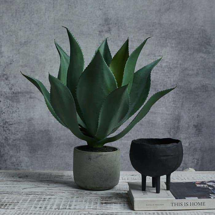 Tall artificial aloe vera planted in a round grey pot next to a black planter