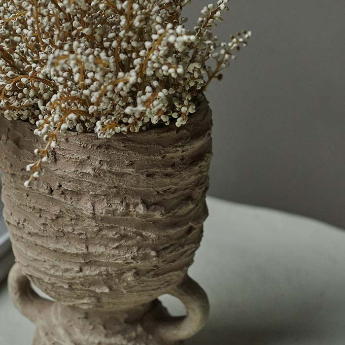Roughly textured brown hourglass shaped vase filled with cream flower stems