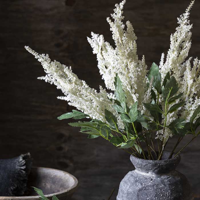 Small bunch of feathery cream Astilbe flower stems with leaves in a grey vase