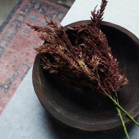 Two artificial red astilbe stems in a wooden bowl.