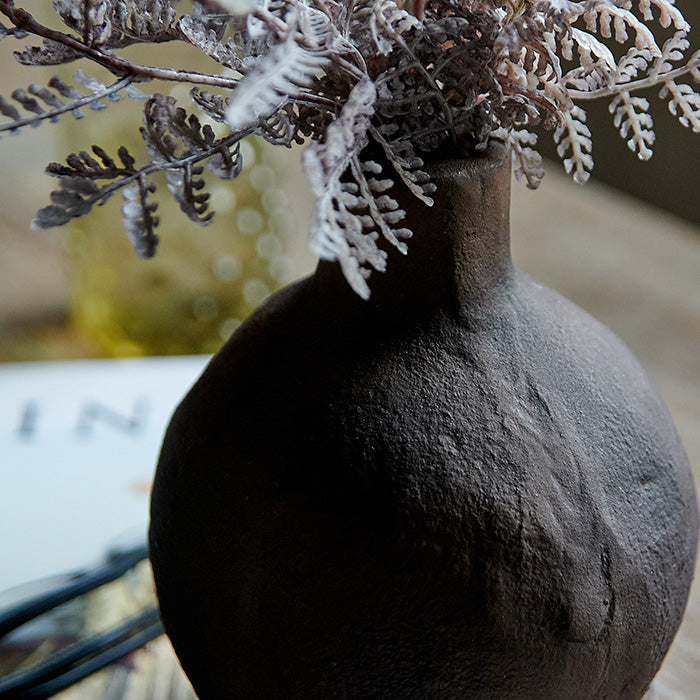 Metal bottle vase in rust-brown colour and rustic texture.