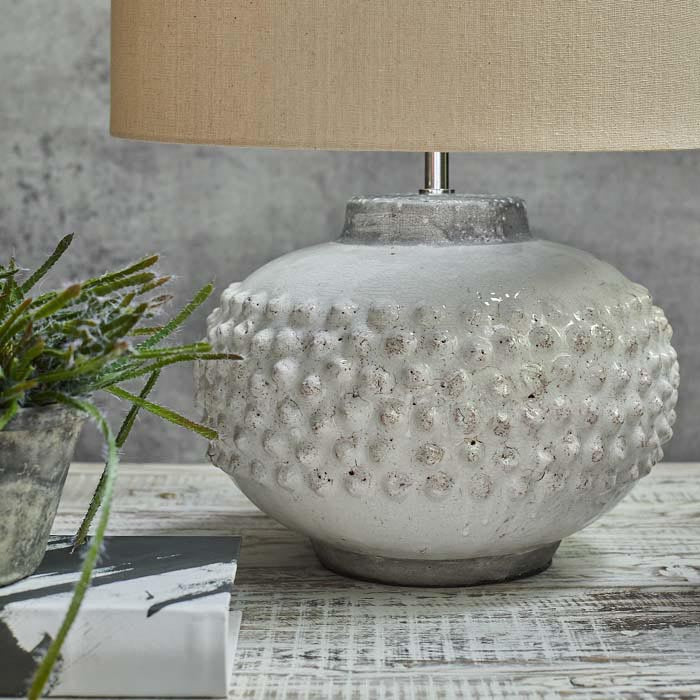 Glossy round white lamp base with a protruding pattern sat on a wooden surface