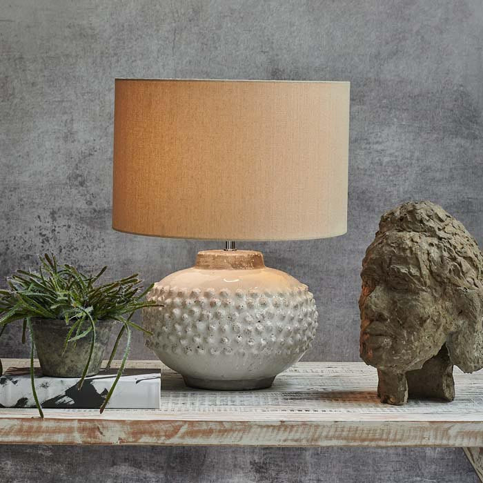 Round cream textured table lamp switched on next to a face sculpture and faux plant