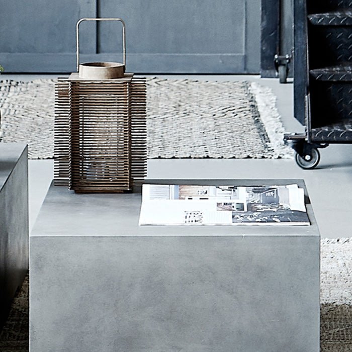 The Beaumont Coffee Table, a grey concrete square coffee table with a cutout leg design, on a sunny patio.