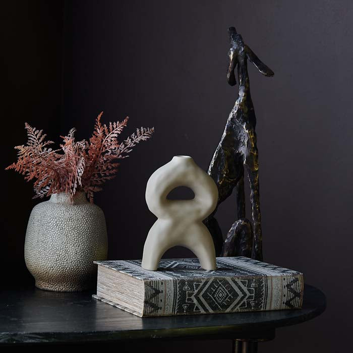 Abstract sculptural cream vase sat on top of a grey patterned storage book