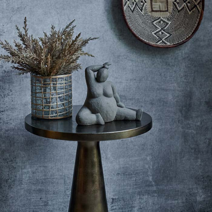 Small cylindrical vase filled with faux flowers sat on a round table next to a grey female sculpture
