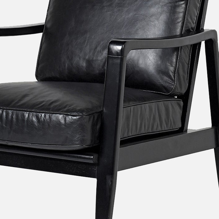 A black leather armchair with a wooden frame with a belt and buckle feature on the back.