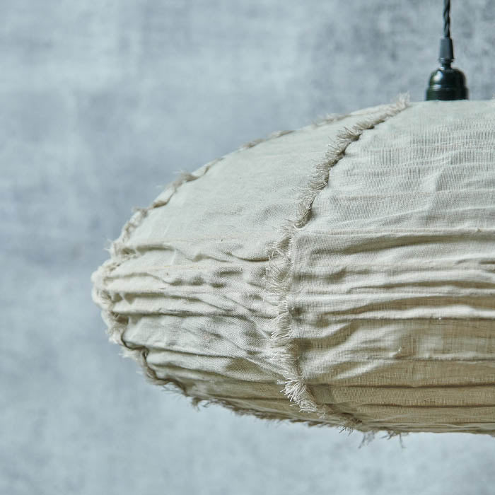 Oval shaped fabric pendant shade hanging from a black cord with tufted edges