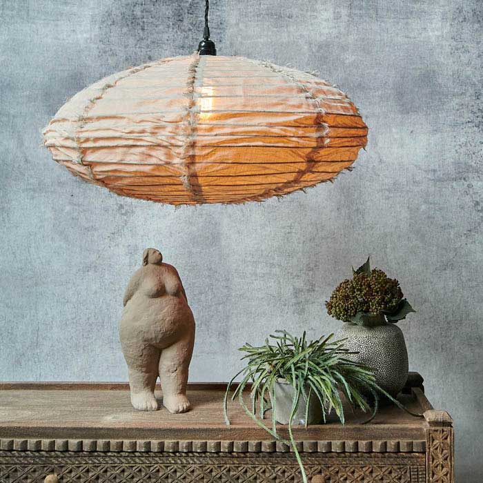Oval shaped cream fabric pendant light hanging from a black cord switched on above a decorated wooden console
