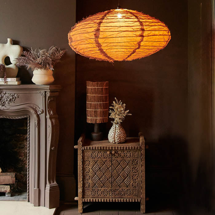 Large oval shaped brown fabric pendant switched on above a carved wooden cabinet