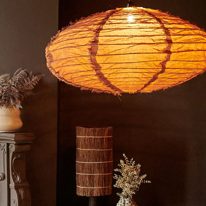 Large oval umber linen lampshade with light bulb glowing through fabric.