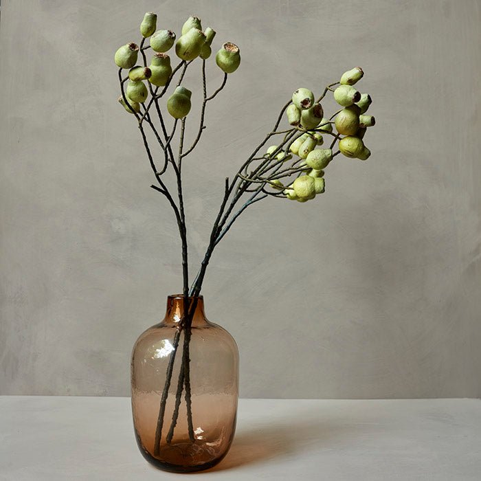 Three artificial stems of eucalyptus gum nut in a brown glass bottle vase.
