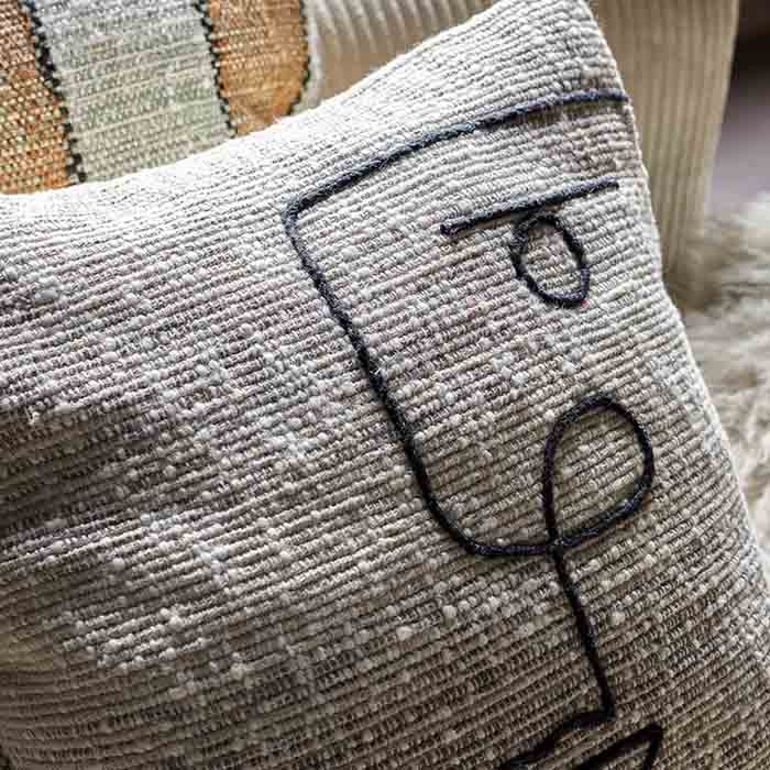 Grey woven cushion with black abstract face design.