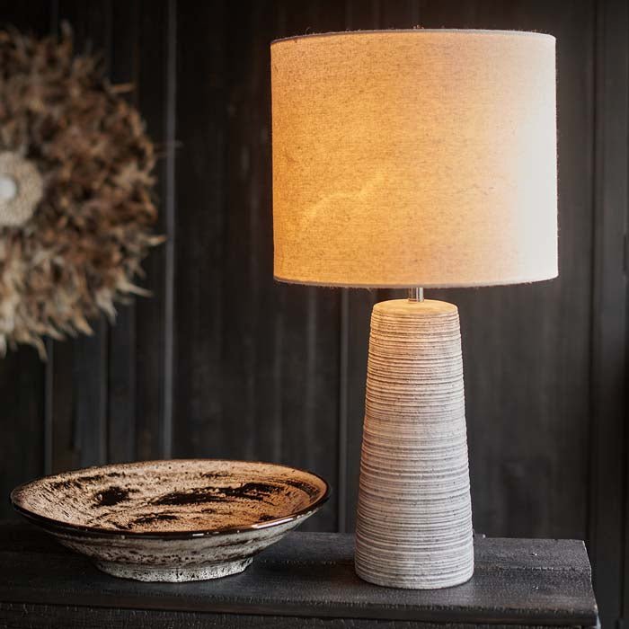 The Fria Table Lamp, warmly lit against a black wall and a feathered wall hanging.