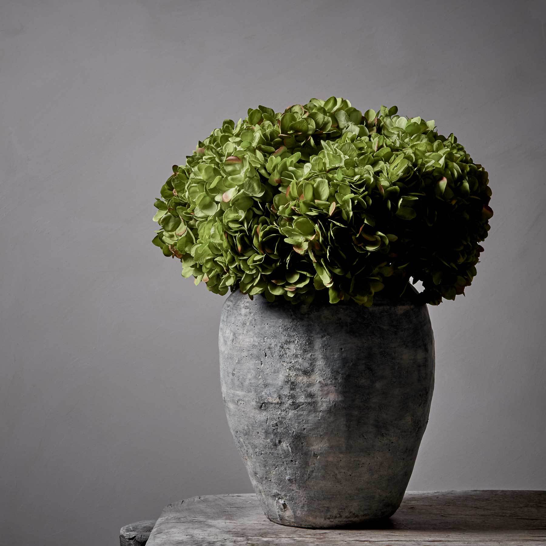 Artificial green hydrangeas in a large grey stoneware vase.